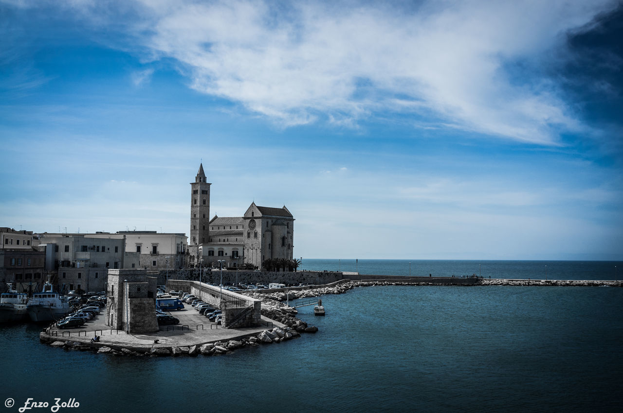 BUILDINGS BY SEA AGAINST CLOUDY SKY