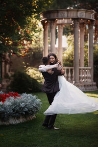 The groom circles the bride in his arms in a beautiful summer garden