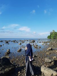 Woman standing on rock against blue sky