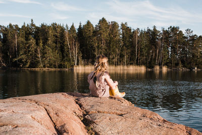 Young girl sat on a rock with a feather headband looking out thinking