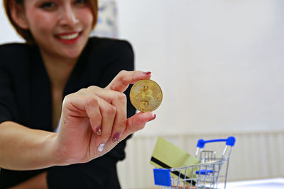 Young businesswoman holding coin with shopping cart and credit card in office 