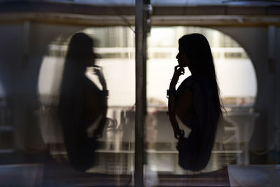 Silhouette man photographing woman standing by window