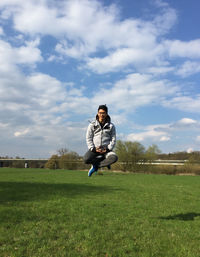Full length portrait of man sitting in mid-air over grassy field against sky