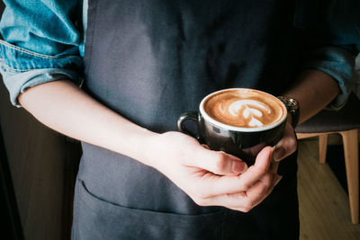 Midsection of woman holding coffee cup on table