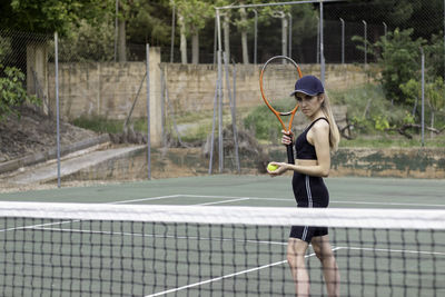 View of young beautiful woman looking to camera prepared to play a tennis match on a green court