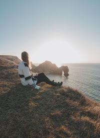 Rear view of woman sitting on beach against clear sky