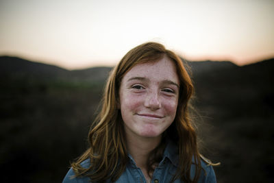 Close-up portrait of smiling girl on field against sky during sunset