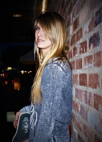 Portrait of a smiling young woman against brick wall