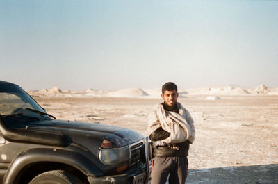 Portrait of young man standing by car on land