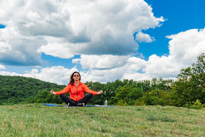 Full length of woman exercising on field against sky