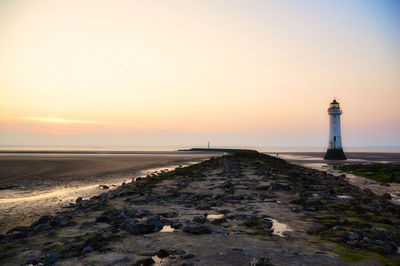 Lighthouse amidst sea and buildings against sky during sunset