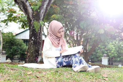 Smiling young woman reading book while sitting at park