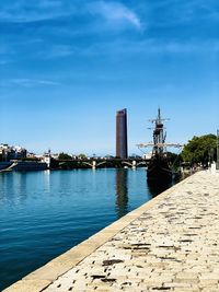 Pier over river by buildings in city against sky