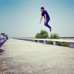 Man jumping on footpath against sky