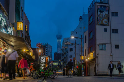 People on illuminated street amidst buildings in city at night