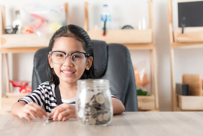 Portrait of girl sitting by coins at home