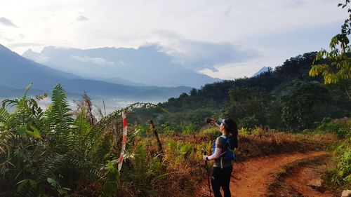 Woman hiking on dirt road against sky