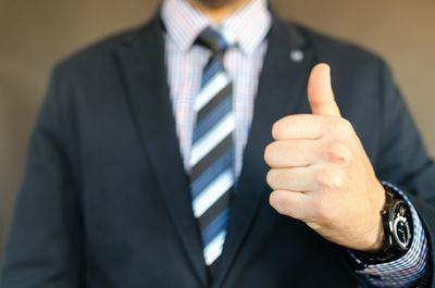 Midsection of businessman gesturing while standing against yellow background