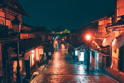 Illuminated street amidst buildings against sky at night