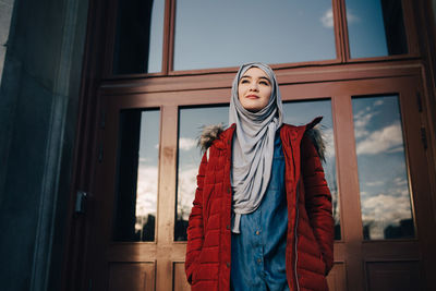 Low angle view of confident young muslim woman standing against entrance door in city