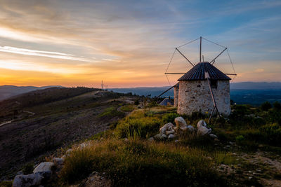 Small windmill on hill against cloudy sky during sunset