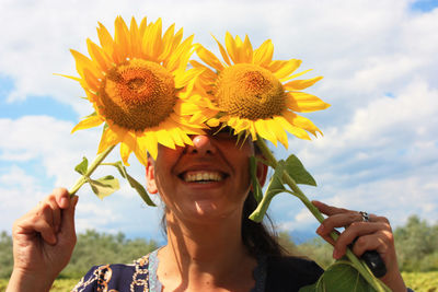 Happy nice woman hides behind yellow blooming sunflowers in summer