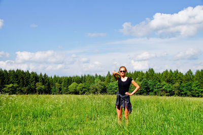 Full length portrait of smiling young woman standing on field