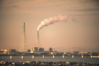 Smoke emitting from chimney by river against sky