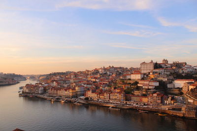 River by cityscape against sky during sunset