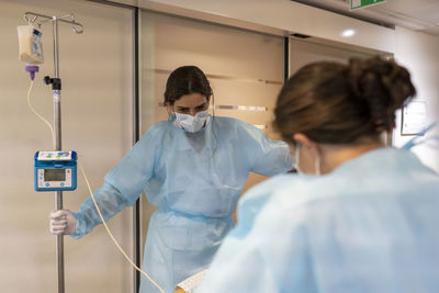 Two nurses help a patient walk in a hallway