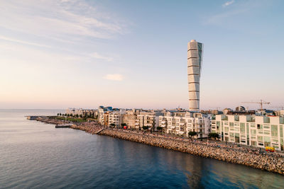 Buildings by sea against sky during sunset