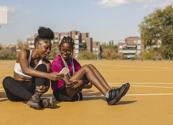 Happy young woman sharing mobile phone with friend at sports court