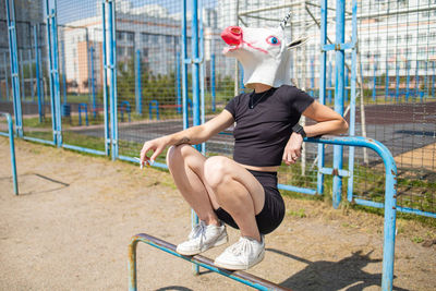 Funny teen girl wear unicorn head sitting in park