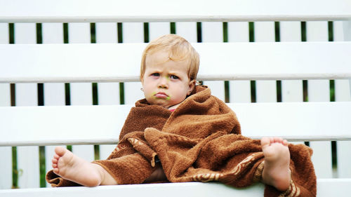 A little one-year-old girl, wrapped in a towel, with a dirty face, lonely sitting on a swing in the