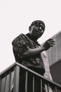 Low angle view of young man standing by railing against clear sky