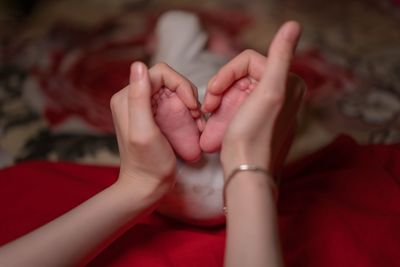 Cropped hands forming heart shape while holding baby feet on bed