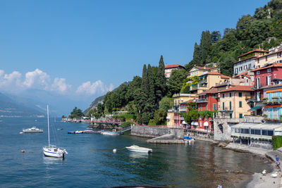 Sailboats moored on sea by buildings in city against sky