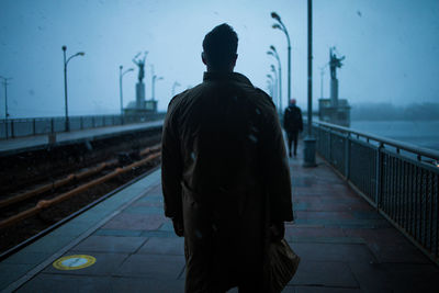 Rear view of man walking on railroad station platform in fog