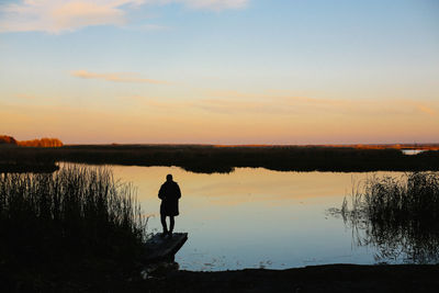 People standing by lake at sunset