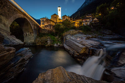 Arch bridge over river by buildings against sky