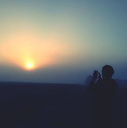 Rear view of silhouette person photographing against clear sky during sunset