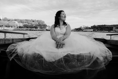 Bride sitting on boat on lake against sky