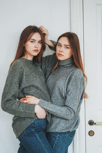 Portrait of sisters standing against wall