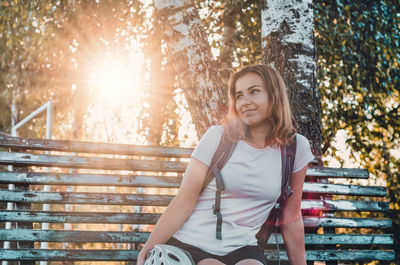 Cheerful pretty girl resting on bench against the background of sun