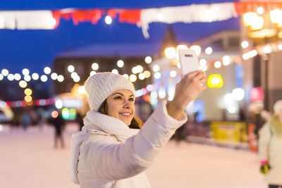 Portrait of smiling woman standing in illuminated park during winter