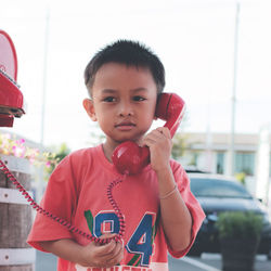 Cute boy talking on phone while standing against clear sky