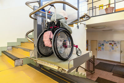 Young child living with cerebral palsy using electric wheelchair lift to access public building.