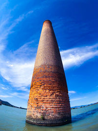 Low angle view of smoke stack by sea against blue sky