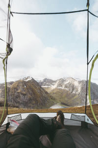 Low section of man lying in tent with mountains in background against sky