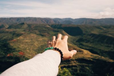 Close-up of man hand gesturing towards mountain against sky